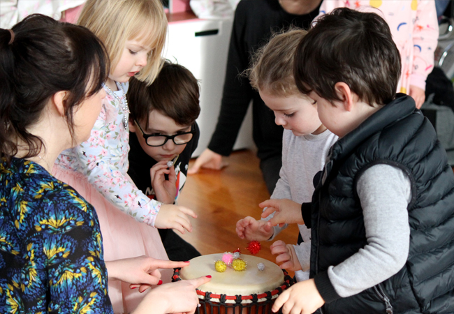 Children surround drum with ELC music class teacher